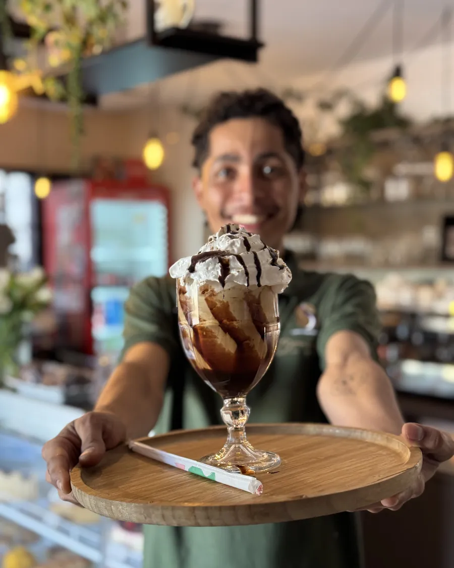 Atendente do Boulevard servindo uma taça com chantilly e calda de chocolate no salão
